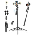 Black selfie stick kit with a telescoping tripod base, smartphone mount, ring light, two microphone attachments, a remote control, and a folded stand, shown on a plain white background.